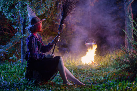 young witch by  fire in night forest makes in cauldron magic potion