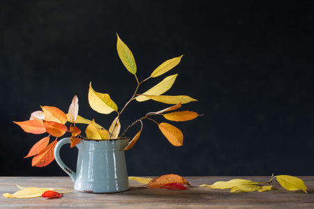 autumn leaves in jug on wooden table on dark backgroundの写真素材