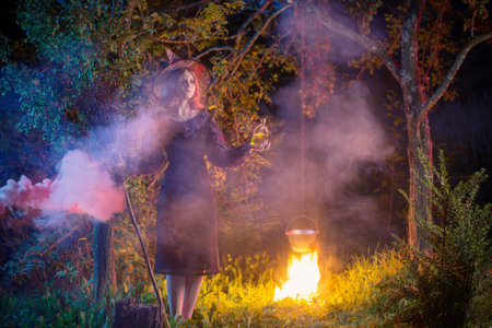 young witch by  fire in night forest makes in cauldron magic potion