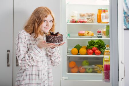 smile teenager girl at fridge with chocolate cakeの写真素材