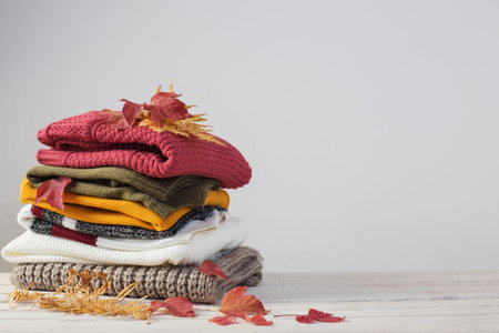 stack of sweaters with autumn leaves  on  white wooden table