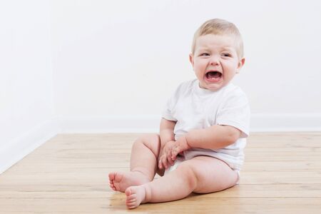 baby crying sitting on wooden floorの写真素材
