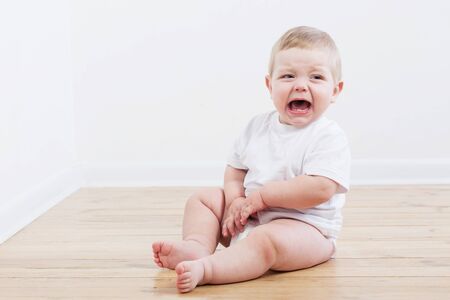 baby crying sitting on wooden floor