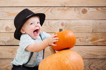baby in black hat with pumpkins on wooden backgroundの写真素材