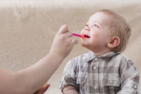 mother feeds  small child with fruit pureeの写真素材