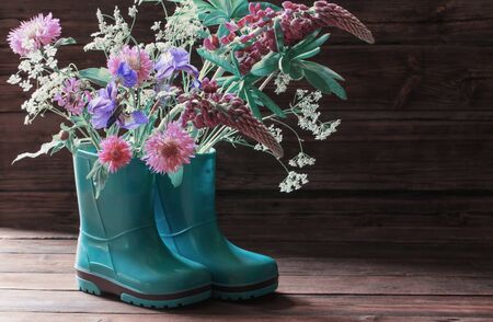 summer flowers in rubber boots on old dark wooden backgroundの写真素材
