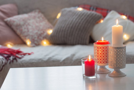 Composition of candles on  white table against the background of  sofa with plaids and pillows. Cozy home conceptの写真素材