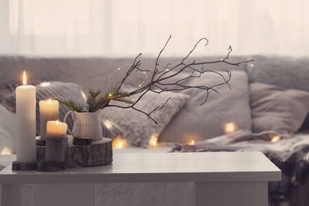 Composition of candles on  white table against the background of  sofa with plaids and pillows. Cozy home conceptの写真素材