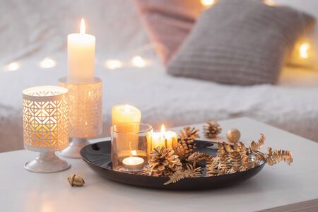 Christmas decoration   with burning candles on  white table against the background of  sofa with plaids and pillows. Cozy home and holiday conceptの写真素材