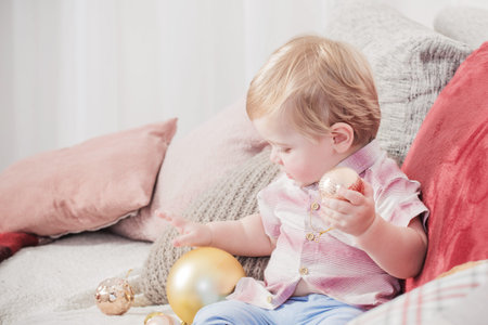 baby with Christmas balls and toys on sofa indoor