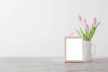 wooden frame and pink tulips in white ceramic vase  on background white wallの写真素材