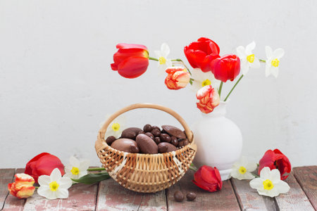 Easter chocolate eggs in basket and spring flowers on old wooden table