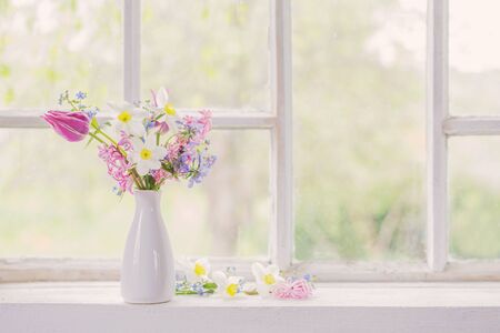 spring flowers in white vase on old windowsillの写真素材