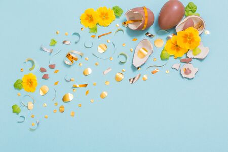 Easter chocolate egg with golden confetti and spring flowers on blue backgroundの写真素材