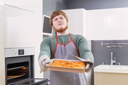 young man with red beard  making  pie on white modern kitchenの写真素材