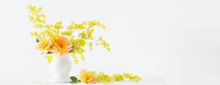 orange roses with wild flowers in bouquet in white vase in interiorの写真素材