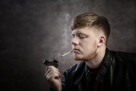 Young man in  leather jacket smokes cigarette on dark background