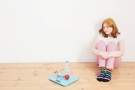 sad teenager girl with scale on wooden floorの写真素材