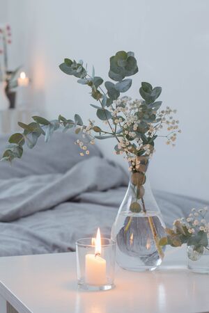 burning candles and eucalyptus in glass vase in white bedroomの写真素材