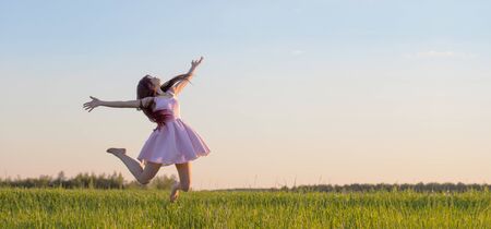 beautiful young girl in pink dress jumping in field の写真素材