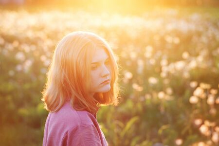 beautiful teenager girl on background dandelions meadow at sunsetの写真素材