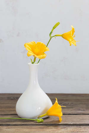 yellow day-lily flowers in white vase on wooden tableの写真素材