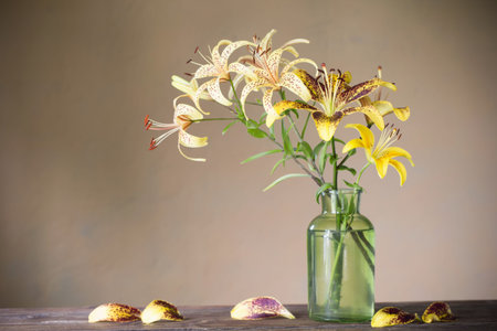 yellow lily in green glass vase on wooden table