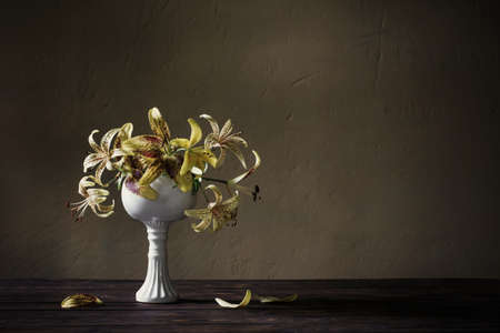 yellow lily in ceramic white vase on wooden table on dark backgroundの写真素材