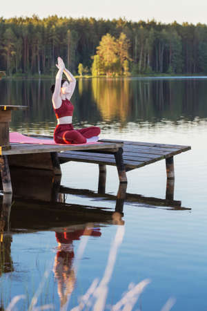 girl doing yoga on wooden pier by lake in summerの写真素材