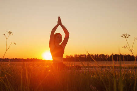 young woman doing yoga at sunset in summerの写真素材