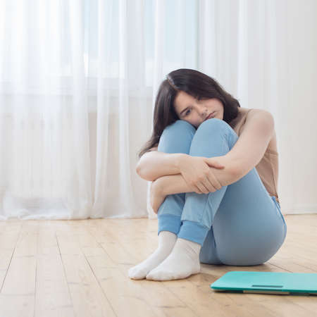 sad teenager girl on floor with scalesの写真素材