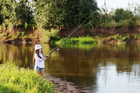 happy little girl with fishing rod on summer riverの写真素材