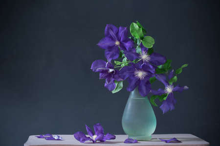 clematis flowers in glass vase on vintage wooden shelfの写真素材