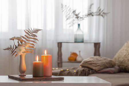 burning candles with autumn decor on white table at homeの写真素材
