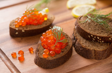 red caviar with black bread, dill and lemon on wooden board