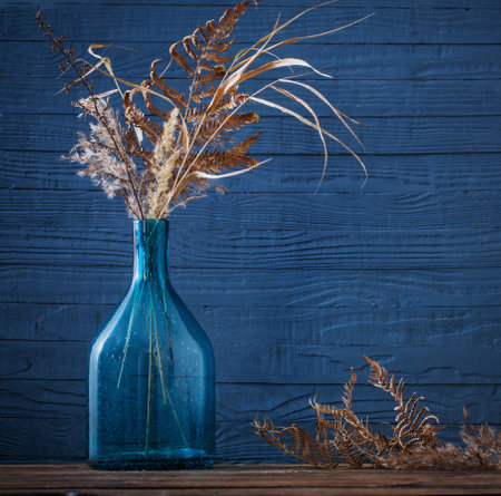 dried flowers in glass vase on wooden table on blue backgroundの写真素材