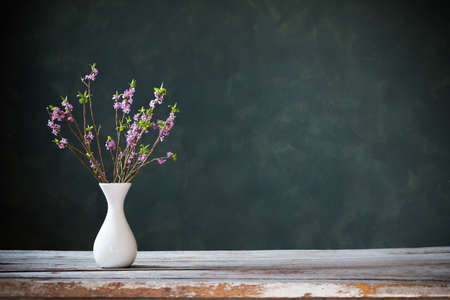 daphne flowers in vase on old wooden table on background green wallの写真素材