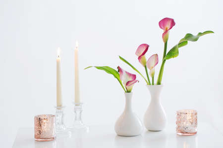 pink calla lily in vase and burning candles on white backgroundの写真素材