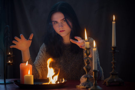 young witch with fire and burning candles on dark background