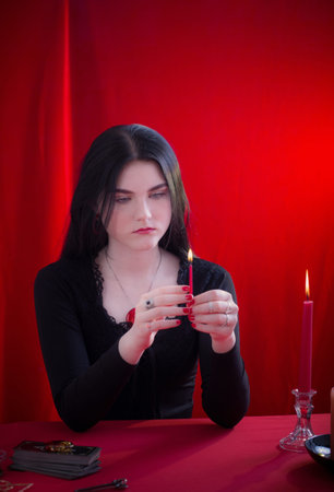 young girl in a black dress is engaged in fortune telling with candles on red backgroundの写真素材