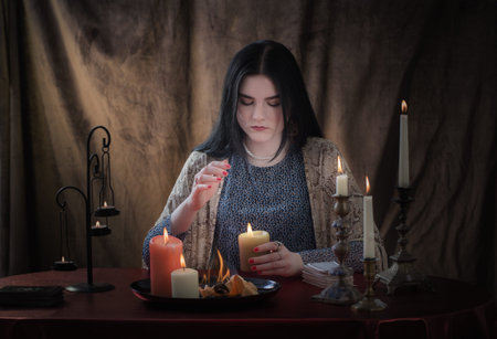 young witch conjures with burning candles on dark background
