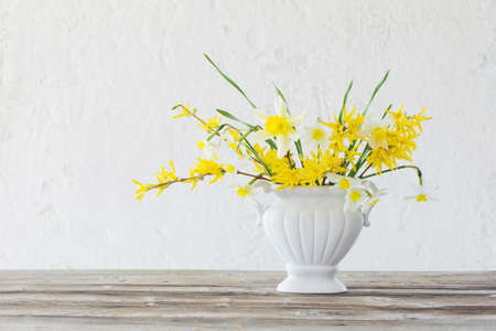 white and yellow spring flowers in vase on background old white wallの写真素材
