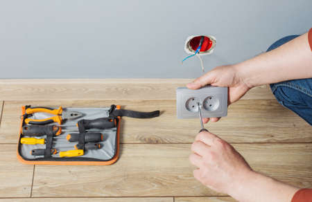 man installs an electrical outlet on gray wallの写真素材