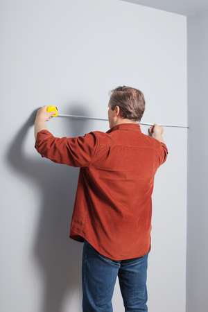 man measures a gray wall with construction tapeの写真素材