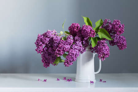 beautiful lilac flowers in white jug on white wooden tableの写真素材