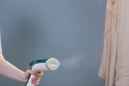 female hand with steamer and shirt on blue backgroundの写真素材