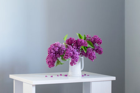 beautiful lilac flowers in white jug on white wooden tableの写真素材