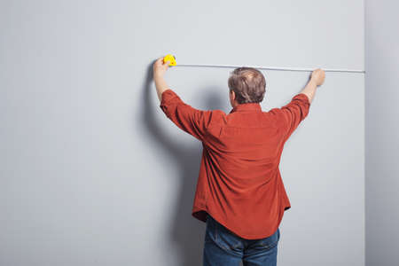 man measures a gray wall with construction tapeの写真素材