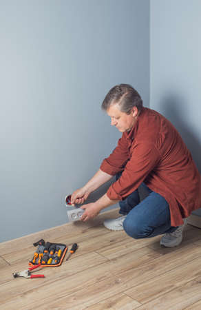 man installs an electrical outlet on gray wallの写真素材