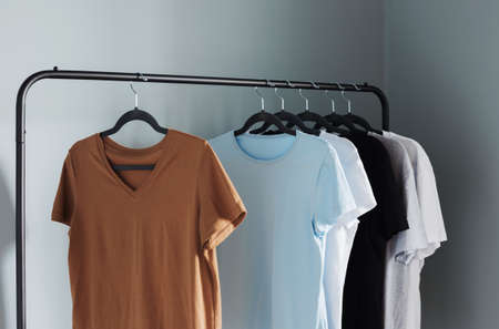 T-shirts of neutral colors on black hanger against gray wallの写真素材